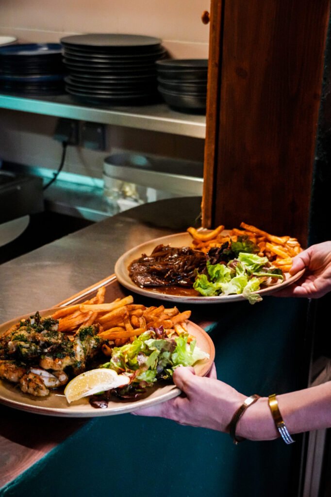 Assiettes de viande grillée, frites et salade prêtes à être servies en cuisine du restaurant La Table de Camille